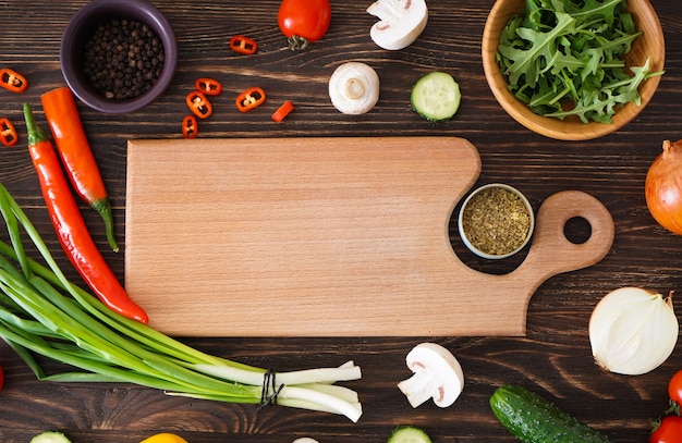 Tabla de cortar de madera e ingredientes frescos para cocinar en el fondo de la mesa de madera, espacio para texto. Endecha plana