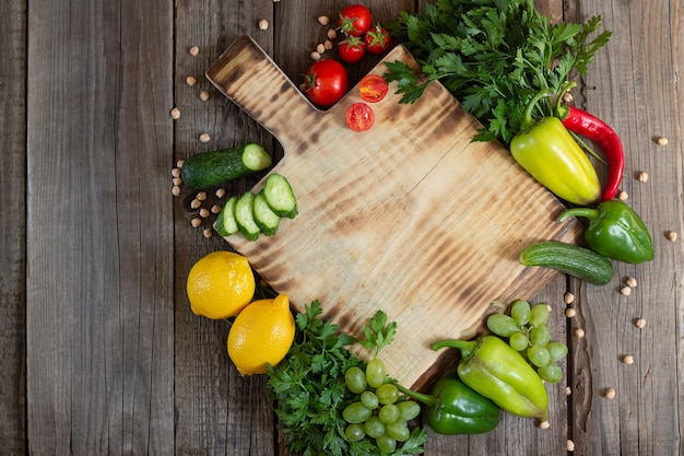 Tabla de cortar de madera con hierbas frescas, verduras crudas y frutas en la vista superior de la mesa de madera rústica