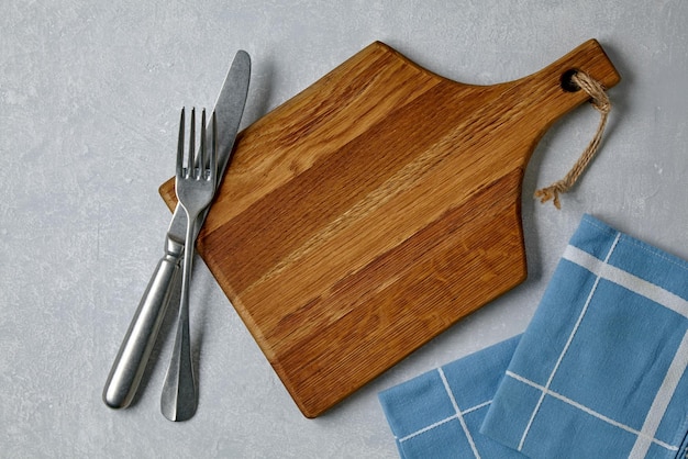 Tabla de cortar de madera marrón con cubiertos y servilletas sobre una mesa de hormigón gris claro Plantilla para colocar los platos Vista superior con espacio de copia Plano