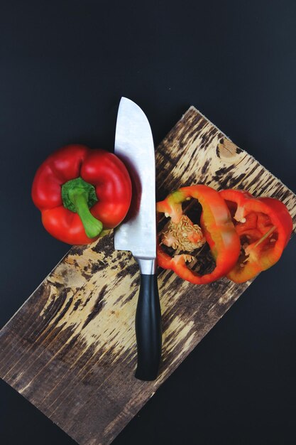 Tabla de cortar de madera con pimienta de verduras crudas en tabla de cortar rústica Pimienta en rodajas y cuchillo con mango de madera en tabla de cortar rústica