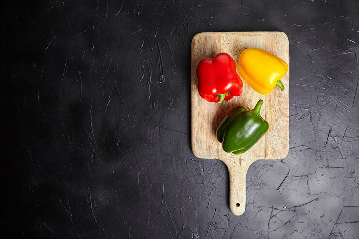 Tabla de cortar de madera de pimientos rojos verdes y amarillos en la mesa de piedra oscura vista superior de alimentos saludables