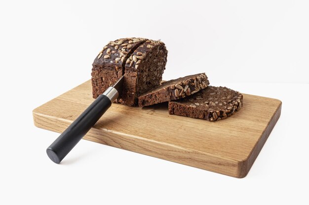Tabla de cortar de madera con rebanadas de pan oscuro y cuchillo aislado sobre fondo blanco.