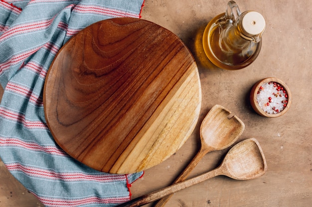 Tabla de cortar de madera sobre una toalla con utensilios en la mesa de la cocina rústica.