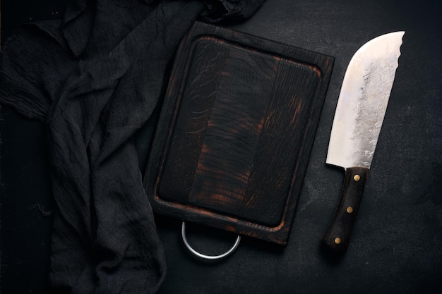 Tabla de cortar de madera vacía rectangular y cuchillo de cocina en mesa negra con vista superior de servilleta de gasa