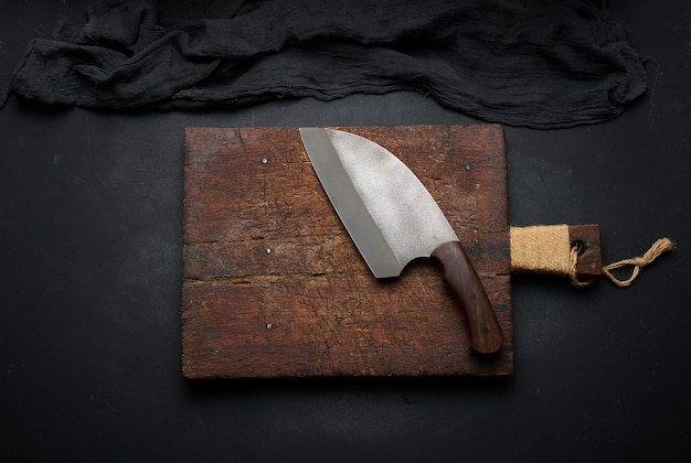 Tabla de cortar de madera vacía rectangular y cuchillo de cocina en mesa negra con vista superior de servilleta de gasa