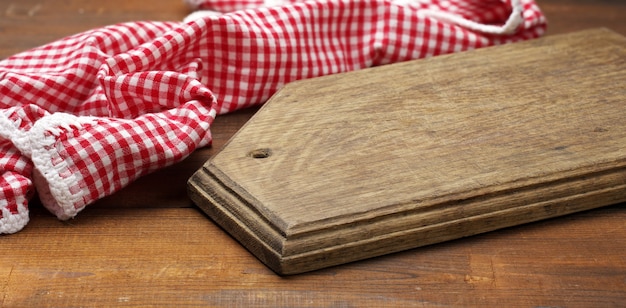 Foto tabla de cortar de madera vieja y servilleta de cocina de algodón rojo y blanco doblado sobre un fondo marrón de madera, vista superior