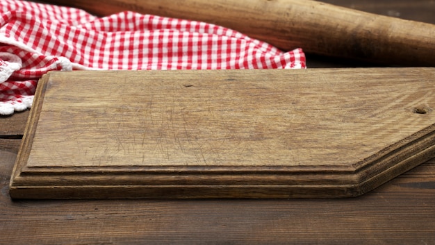 Tabla de cortar de madera vieja vacía y servilleta de cocina de algodón rojo y blanco doblado sobre un fondo marrón de madera, vista superior