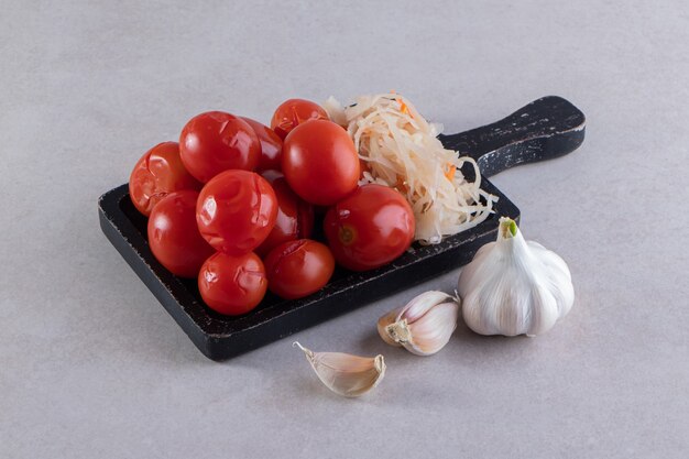 Tabla de cortar negra de tomates en escabeche y repollo sobre piedra.