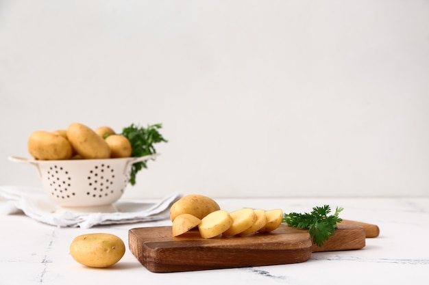 Tabla de cortar con patatas crudas y perejil en mesa