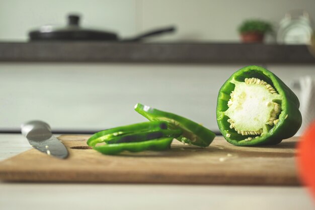 Tabla de cortar con pimientos verdes sobre un fondo de cocina moderna. Pimientos en rodajas sobre tabla de madera. Ingrediente vegetal, cocinar comida sana concepto