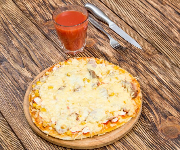 Tabla de cortar con pizza fresca y vaso de jugo de tomate en la mesa de madera