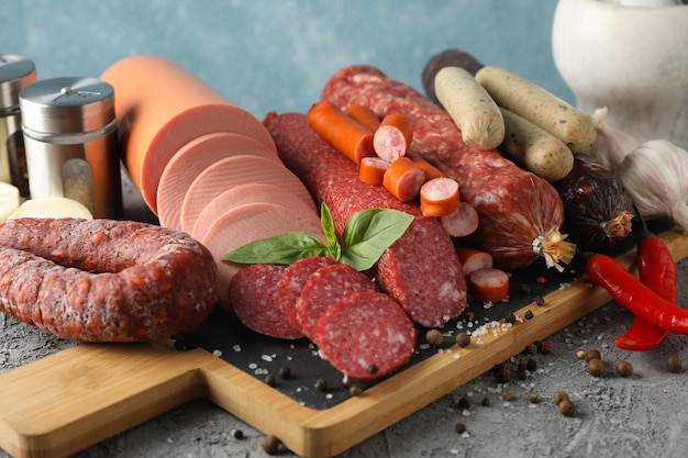 Tabla de cortar con salchichas y especias en mesa gris, de cerca