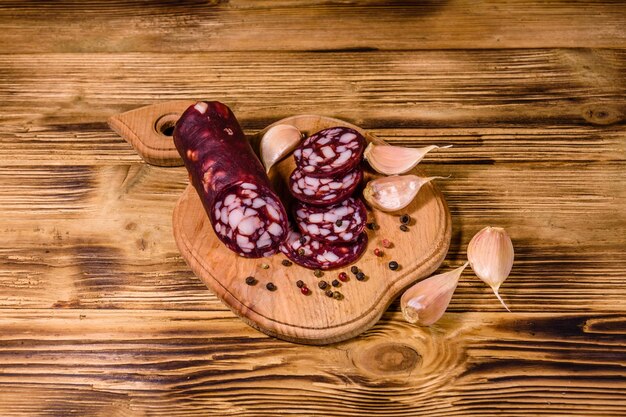 Tabla de cortar con salchichas de salami en rodajas y ajo sobre una mesa de madera rústica