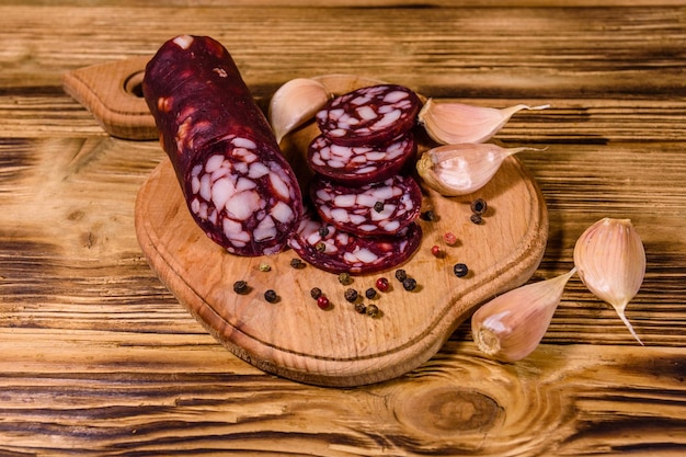 Tabla de cortar con salchichas de salami en rodajas y ajo sobre una mesa de madera rústica