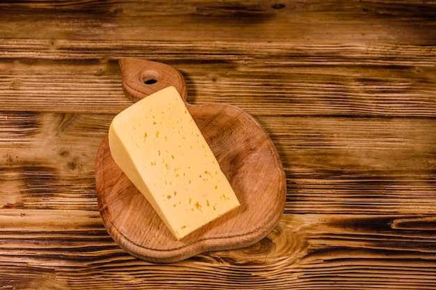 Tabla de cortar con trozo de queso sobre mesa de madera