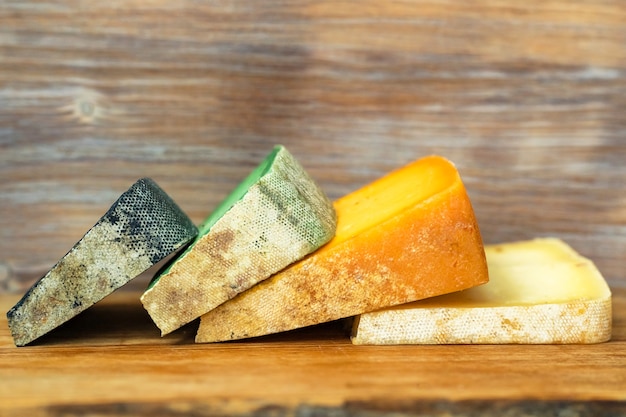 Tabla de cortar con trozos de queso de diferentes colores sobre fondo de pared de madera