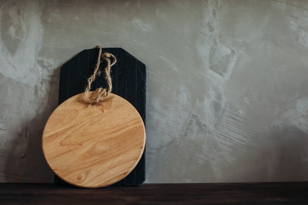 Una tabla de cortar vacía en la cocina en la mesa de madera contra la pared gris