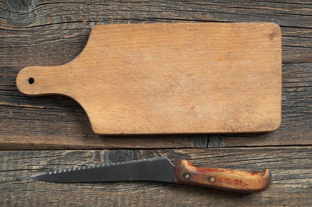 Tabla de cortar vacía y cuchillo en la mesa de madera antigua, vista superior. Fondo de alimentos