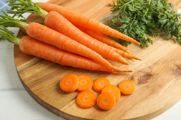 Tabla de cortar con zanahorias maduras en mesa de madera