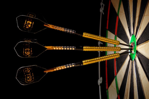 Foto tabla de dardos de sisal con tres dardos en un objetivo en un fondo negro