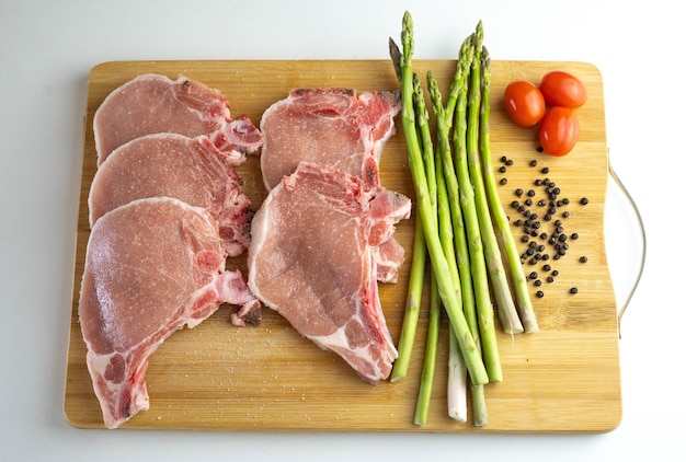 Una tabla de madera con chuletas de cerdo, espárragos y tomates cherry