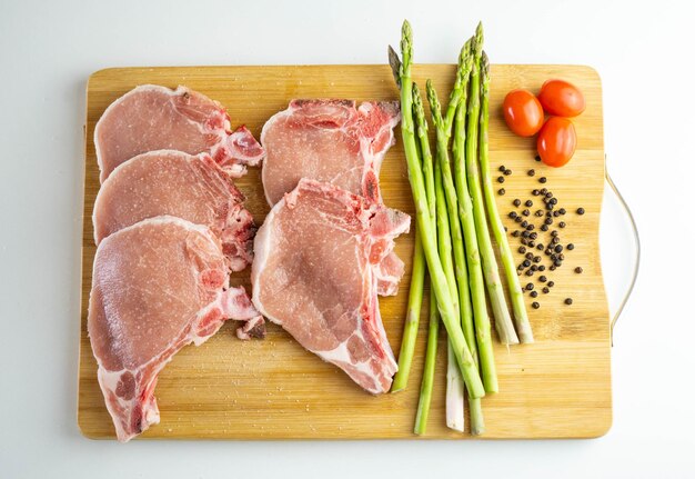 Una tabla de madera con chuletas de cerdo, espárragos y tomates cherry