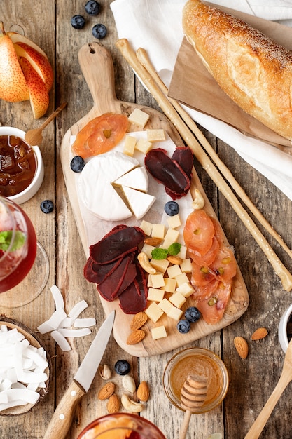 Tabla de madera con diferentes tipos de quesos, carnes, frutas, nueces, baguette en una mesa de madera.Estilo rústico.Fiesta de degustación francesa.