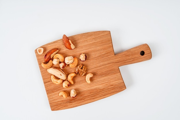 Tabla de madera con nueces, avellanas y anacardos sobre un fondo blanco, el concepto de saludable