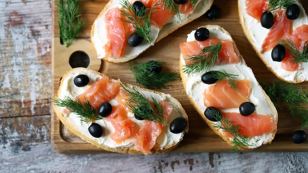 Una tabla de madera con pan, salmón ahumado y aceitunas negras.