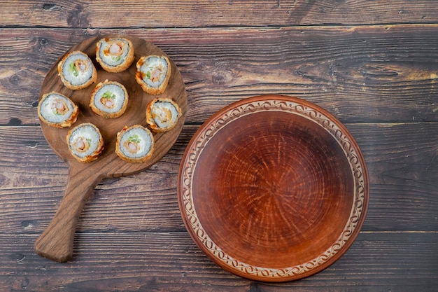 Una tabla de madera de rollos de sushi con camarones, aguacate, queso, tortilla empanizada.