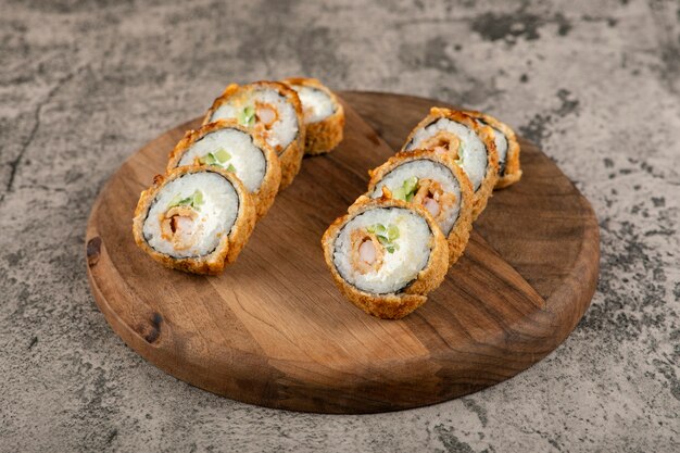 Foto tabla de madera de rollos de sushi frito caliente con salmón sobre superficie de piedra.