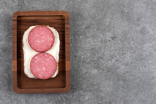 Tabla de madera de tostadas con salami colocado sobre piedra.