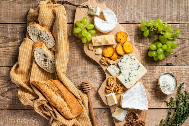 Tabla de quesos. Brie, camembert, roquefort, parmesano y queso crema azul con uva, higo, pan y nueces sobre tabla de madera. fondo de madera. Vista superior.