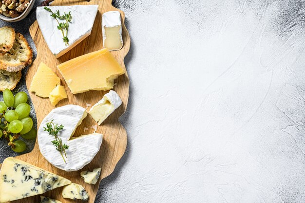 Tabla de quesos con camembert francés, brie, queso parmesano y queso azul, uvas y nueces. Fondo blanco. Vista superior. Copia espacio