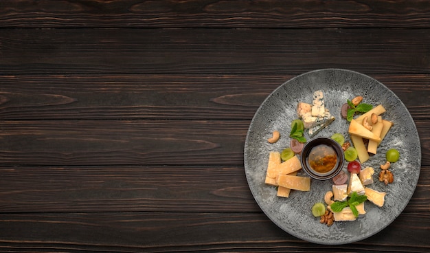 Tabla de quesos con uvas y miel en un plato sobre la mesa de madera.