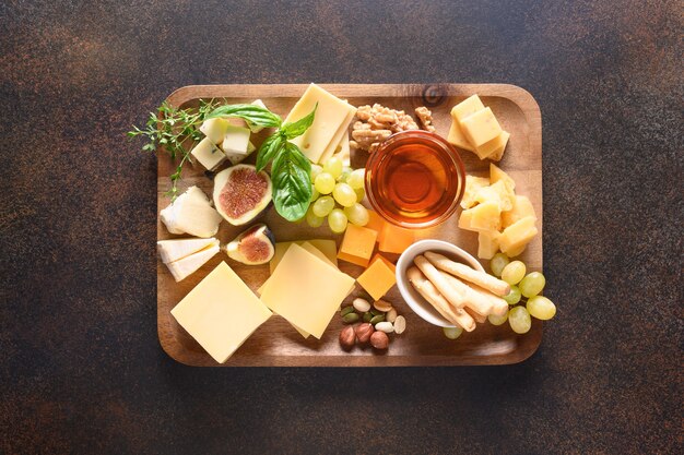 Foto tabla de quesos con uvas nueces higos sobre fondo marrón vista superior