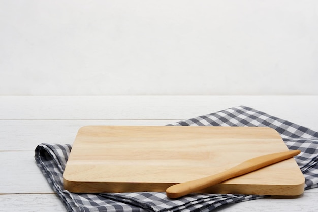 Tabla rectangular de madera para servir con cuchillo de mantequilla y mantel de algodón a cuadros gris sobre mesa de madera blanca