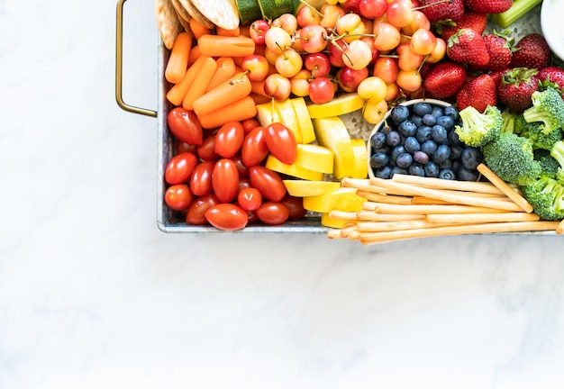 Tabla de refrigerios con frutas frescas, verduras, galletas saladas y salsas para mojar.