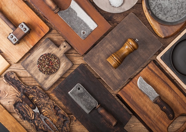 Tablas de cortar de cocina de diferentes tamaños y formas sobre fondo de madera con hachas de carne, tenedor y cuchillo y otros utensilios.