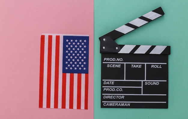 Tablero de azote de película y bandera de Estados Unidos sobre un fondo pastel azul-rosa. Cine, producción de películas, industria del entretenimiento. Vista superior