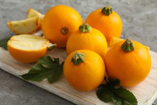 Tablero con calabacín redondo y hojas sobre superficie gris