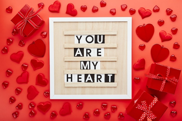 Tablero de cartas con corazones y cajas de regalo sobre fondo rojo Vista superior Fondo para el día de San Valentín