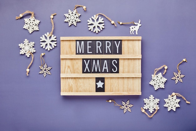 Foto tablero de cartas con texto feliz navidad con decoración navideña sobre fondo violeta flatlay
