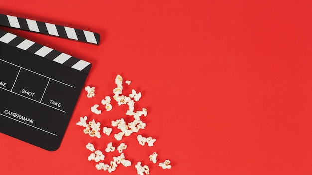 Tablero de Clapper negro o pizarra de película y palomitas de maíz sobre un fondo rojo. Nuevo