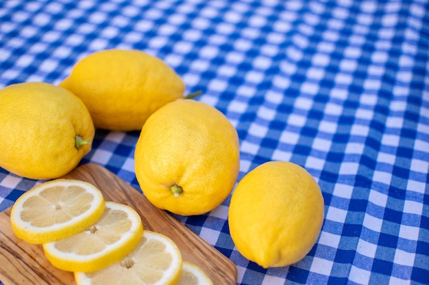 Tablero de cocina de madera con rodajas de limón y limones sobre un mantel a cuadros azul