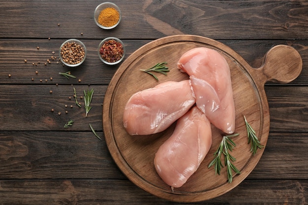 Tablero con filete de pollo crudo sobre fondo de madera