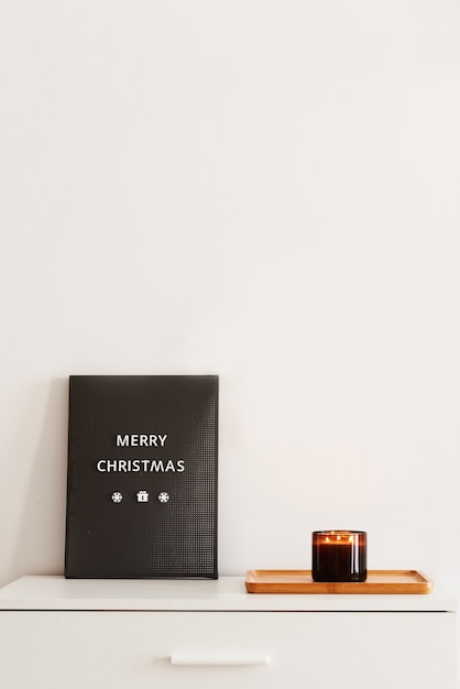 Tablero de letras con frase Feliz Navidad y bandeja con vela aromática ardiente