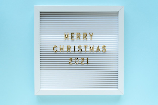 Tablero de letras con saludo Feliz Navidad 2021, decoraciones sobre fondo azul pastel. Composición navideña. Vista superior