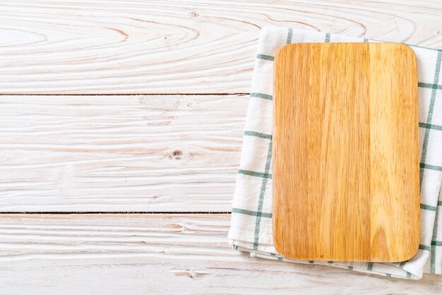Tablero de madera de corte vacío con paño de cocina sobre fondo de madera, vista superior