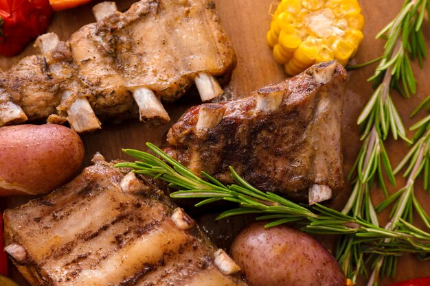 Foto tablero de madera con costillas a la parrilla y verduras closeup